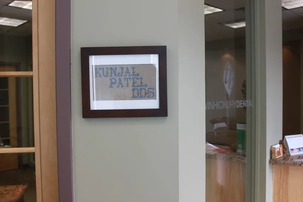 A framed, hand-stitched Kunjal Patel DDS nameplate on the wall inside Twin Hickory Dental.